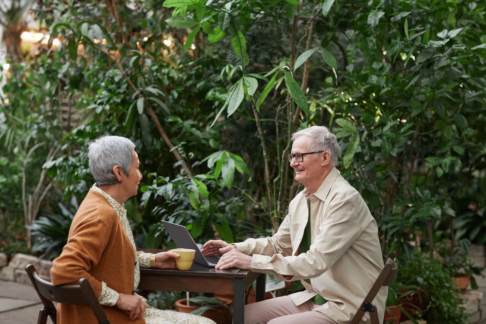Two residents enjoying coffee and conversation at a garden table surrounded by greenery